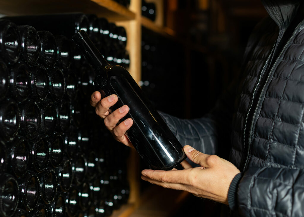 Homme tanant une boutielle de vin sans étiquette dans une cave