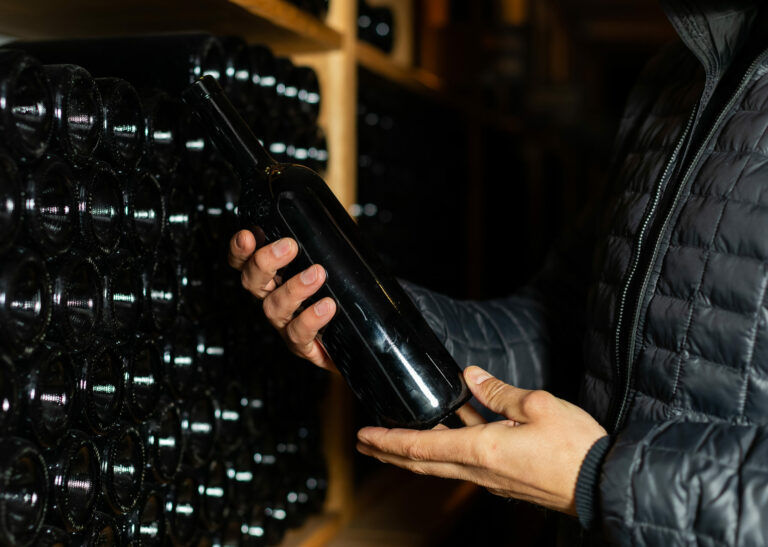 Homme tanant une boutielle de vin sans étiquette dans une cave