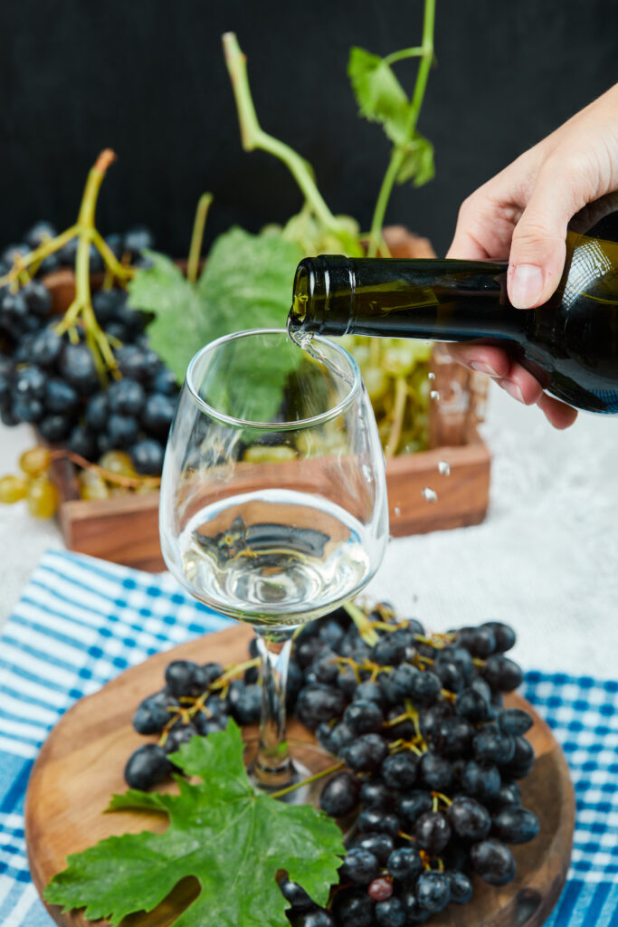 Gros plan sur un verre de blanc posé sur une planche en bois et entouré de raisin